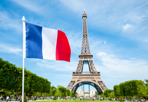 French flag flying in bright blue sky above the Eiffel Tower in Paris, France