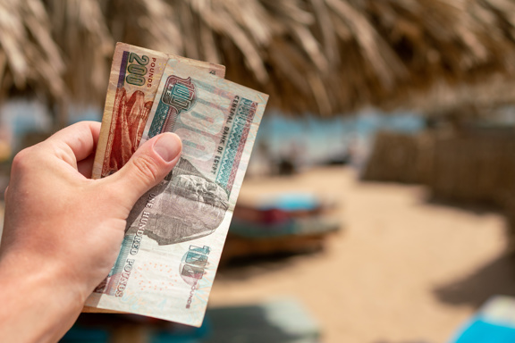 Egyptian pound notes in a man's hand with the beach in the background
