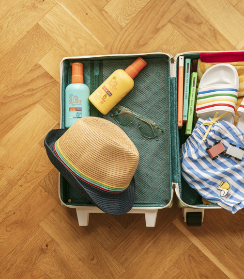 An open suitcase with a hat, flip flops and sunscreen inside