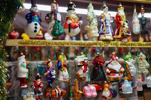 Colourful glass Christmas ornaments, including snowmen, Santas, and festive figures, hanging on display at a market stall.