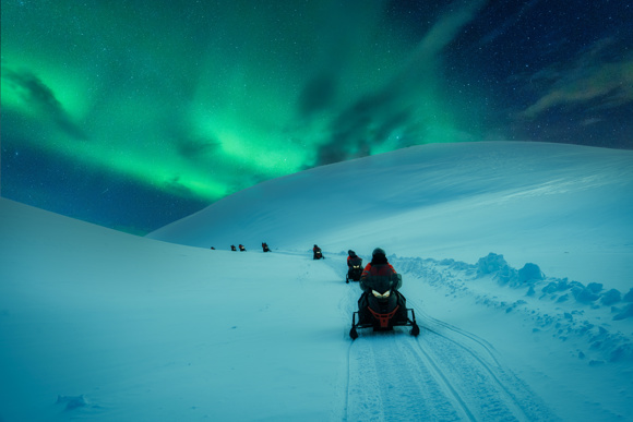 Snowmobiles in the mountains below the Northern Lights